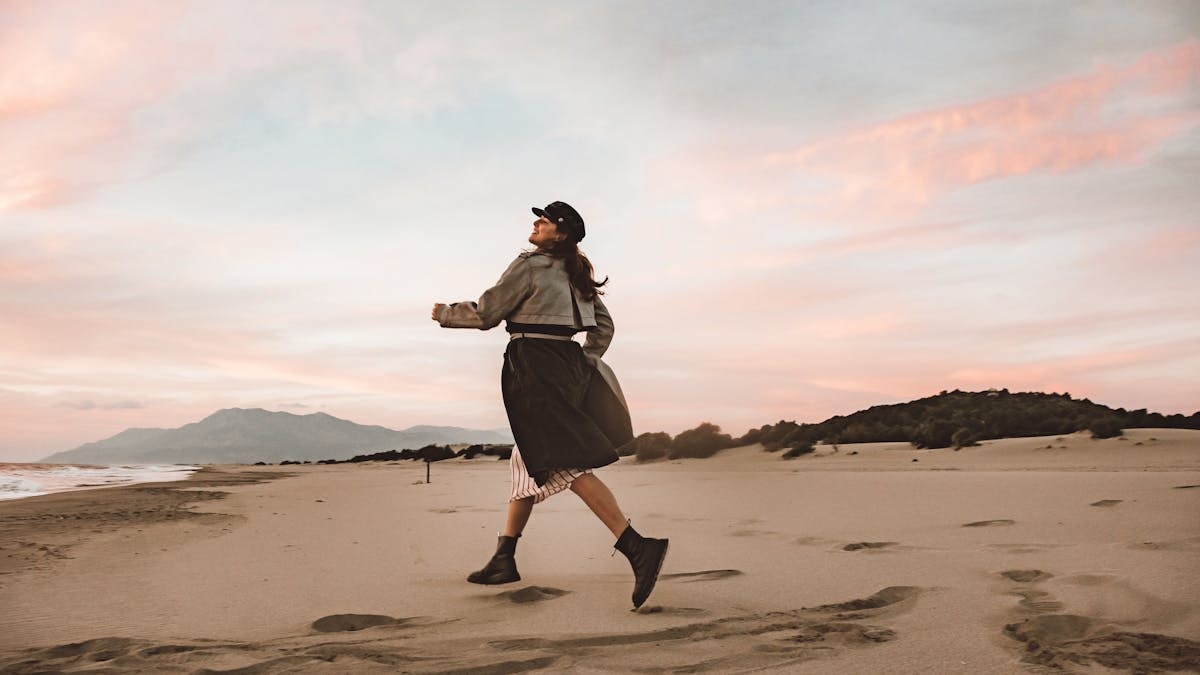 A woman in motion with a backdrop of sand and a colorful sunset sky.